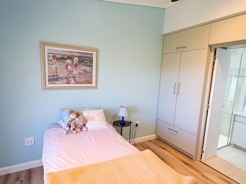 A well-maintained bedroom featuring light blue walls, laminate flooring, a ceiling fan, and a built-in wardrobe with direct access to an en-suite bathroom.