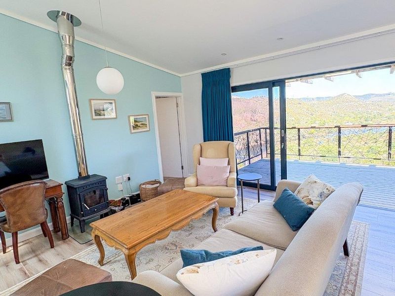 Bright living room featuring a wood-burning stove, ceiling fan, and large sliding glass doors opening onto a deck with scenic mountain views.