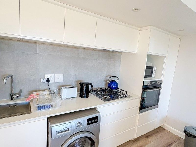 Modern kitchen featuring white cabinetry, stone countertops, integrated gas hob, built-in oven, and space for a washing machine with wood-look laminate flooring.