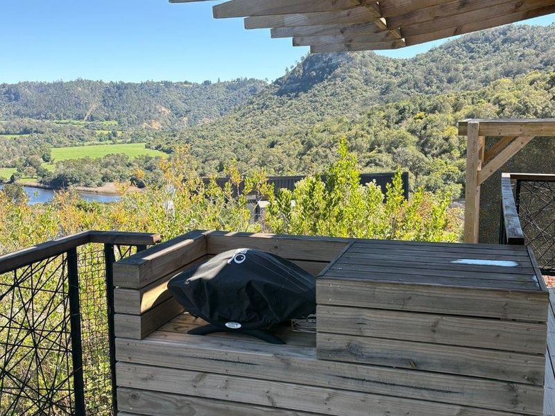 An elevated timber balcony featuring a built-in barbecue station, pergola, and expansive scenic views of the surrounding hills and landscape.