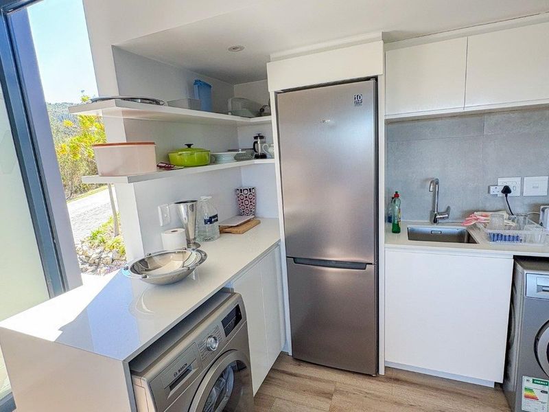 Modern compact kitchen featuring sleek white cabinetry, stone countertops, integrated shelving, and large windows providing ample natural light.