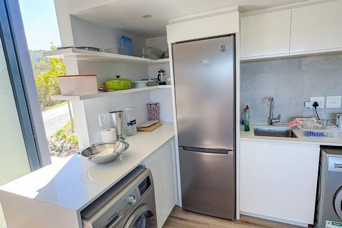 Modern compact kitchen featuring sleek white cabinetry, stone countertops, integrated shelving, and large windows providing ample natural light.