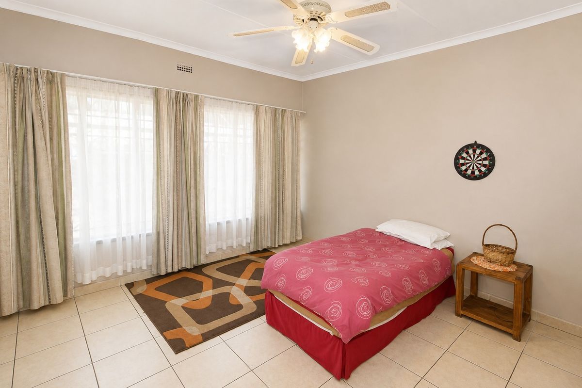 A well-lit bedroom featuring neutral wall tones, tiled flooring, and a ceiling fan, offering a clean and functional space.
