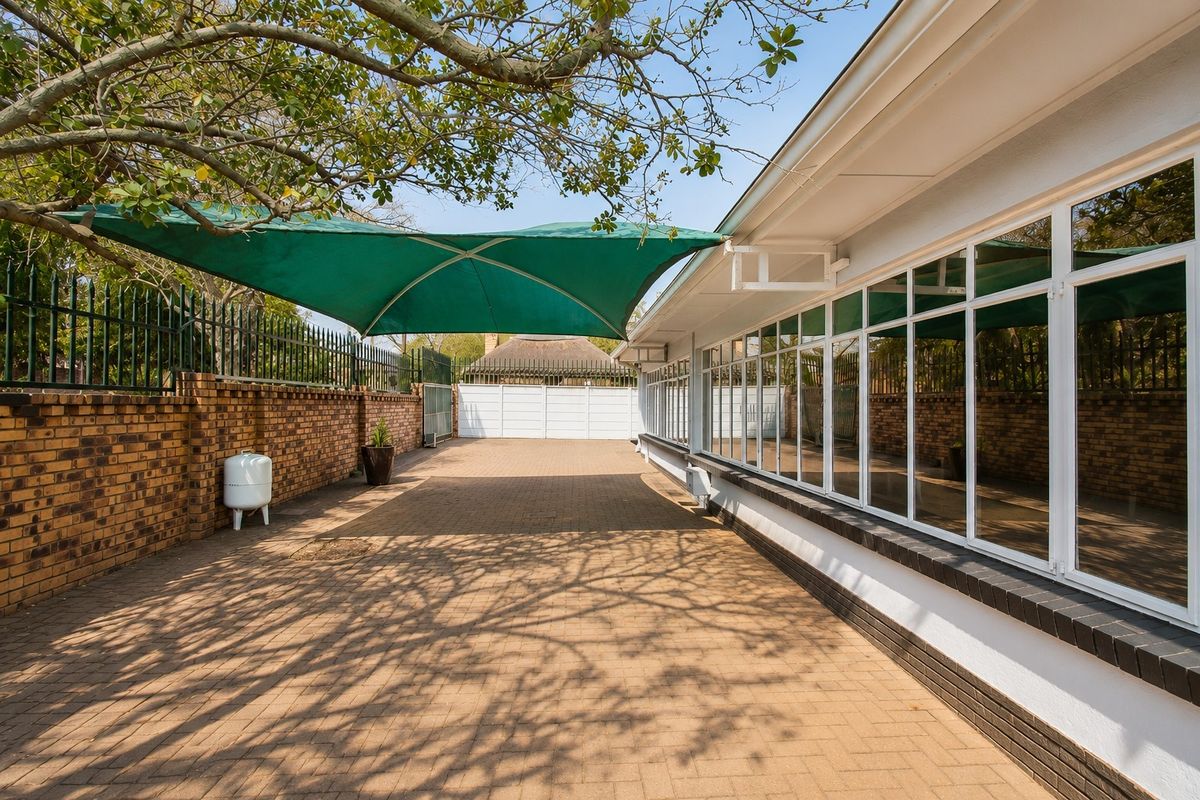 A well-maintained paved rear courtyard featuring a shade sail, brick boundary walls, and large windows providing ample natural light to the interior.
