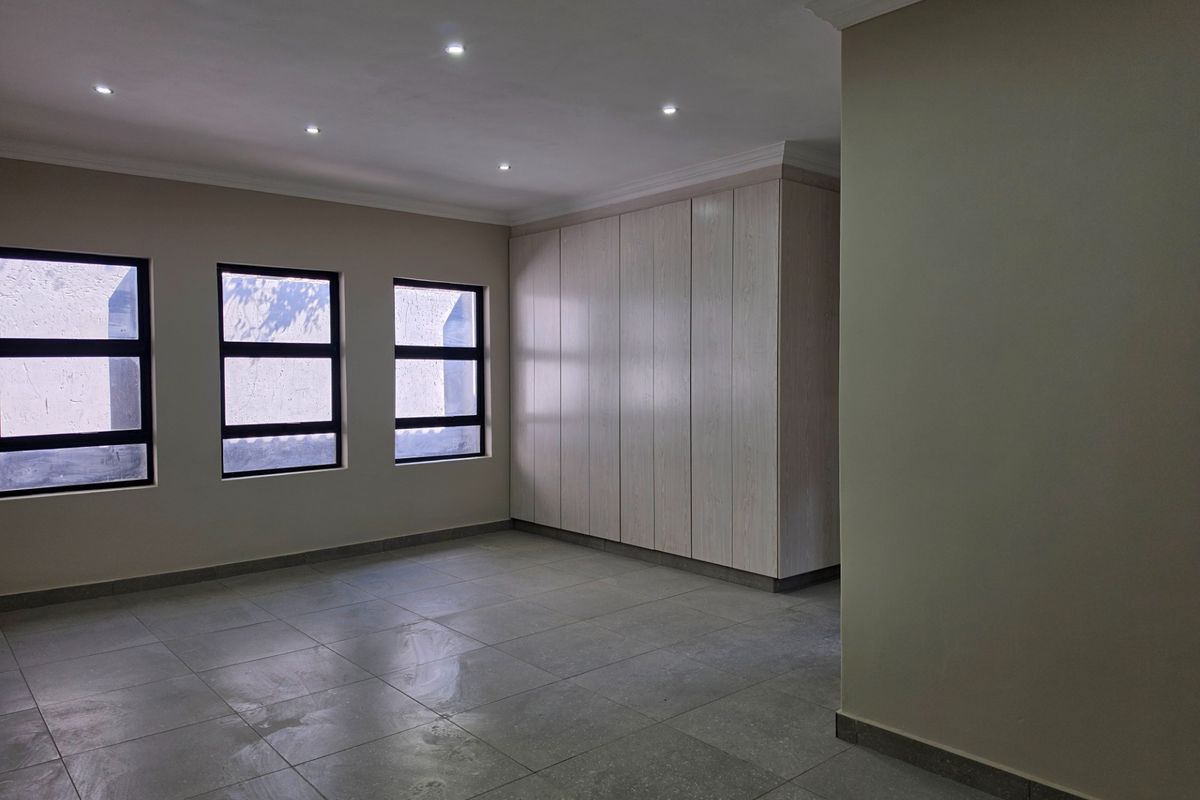 A spacious, empty bedroom featuring neutral tiled flooring, recessed downlighting, and extensive built-in cabinetry with a clean, modern finish.