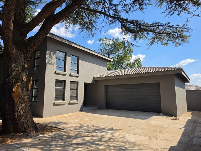 Modern double-storey home exterior featuring a neutral grey facade, tiled roof, large aluminium windows, and an integrated automated garage.
