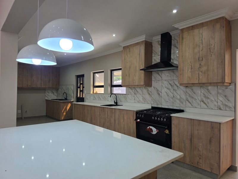 Modern kitchen featuring wood-grain cabinetry, stone countertops, marble-look backsplash, and high-end black appliances, including a gas stove and extractor fan.