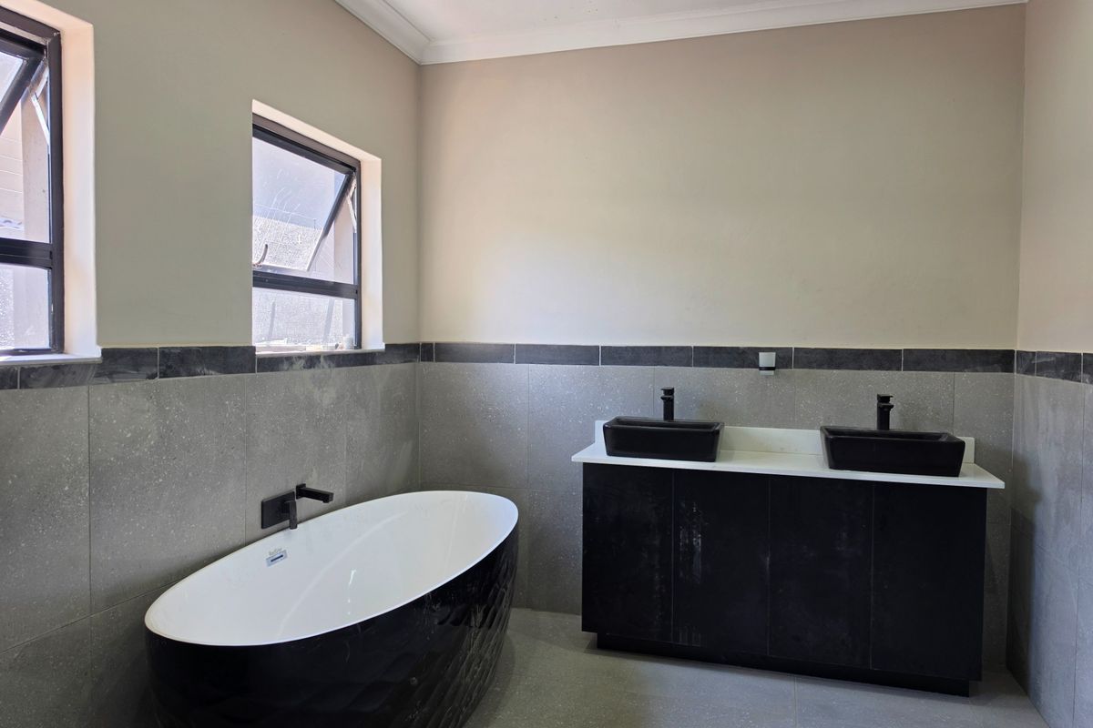 Modern bathroom featuring a sleek black freestanding bathtub, double vanity with black basins, and contemporary grey wall tiling.