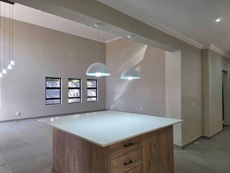 Spacious open-plan area featuring a modern kitchen island with stone countertop, pendant lighting, and neutral tiled flooring throughout.