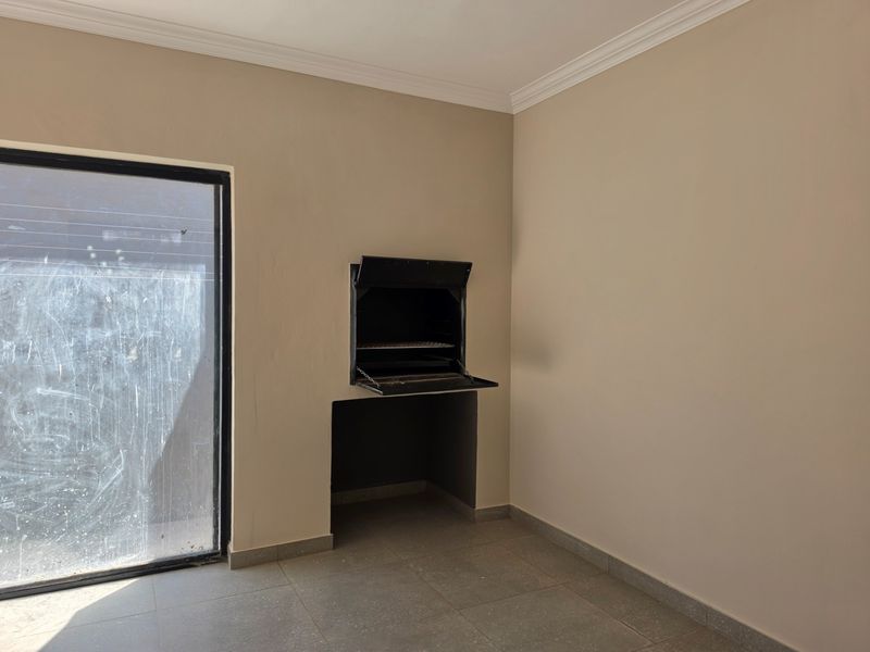 An empty covered patio area featuring a built-in braai, tiled flooring, and a large sliding glass door leading to the exterior.