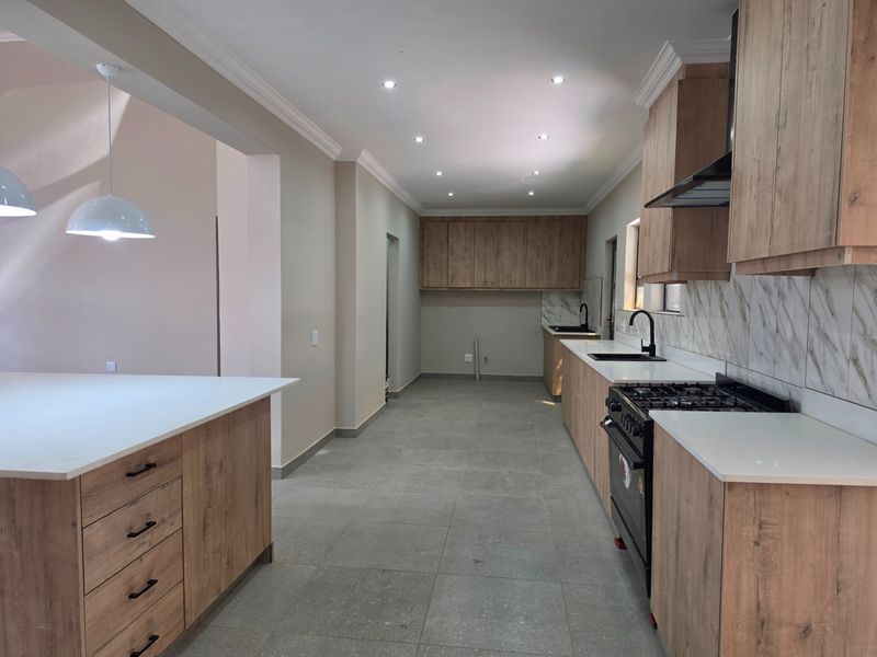 Modern kitchen featuring wood-finish cabinetry, stone countertops, gas stove, extractor fan, and tiled flooring in an open-plan layout.