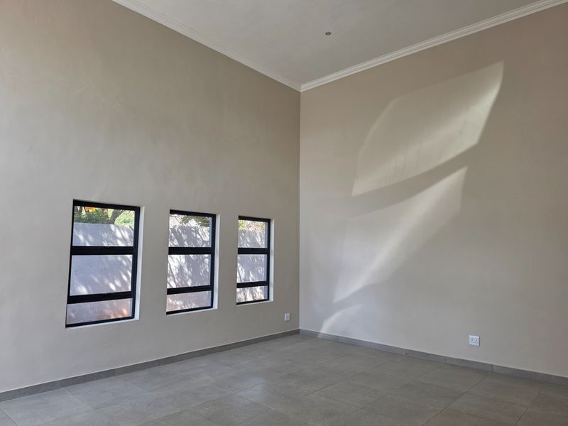 A bright, empty living area featuring neutral walls, tiled flooring, and three modern aluminium-framed windows that allow for natural light.