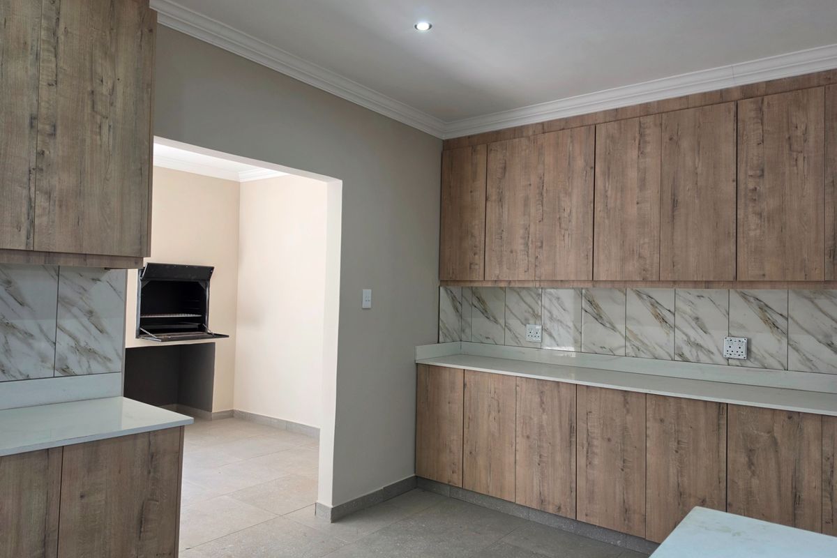 Modern kitchen featuring wood-look cabinetry, stone countertops, and marble-look backsplash, with an adjacent room containing a built-in braai.