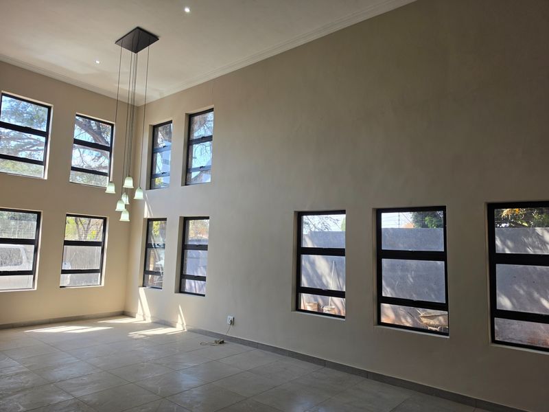 Spacious double-volume living area featuring large aluminium-framed windows, neutral tiled flooring, and modern pendant lighting, offering a bright and airy atmosphere.