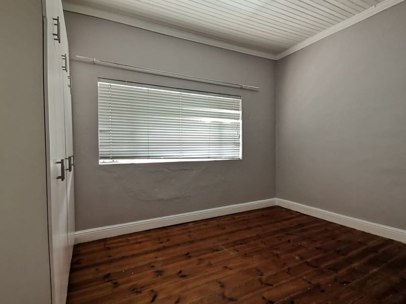 An empty bedroom featuring timber flooring, built-in cupboards, and a tongue and groove ceiling, requiring minor wall repairs.