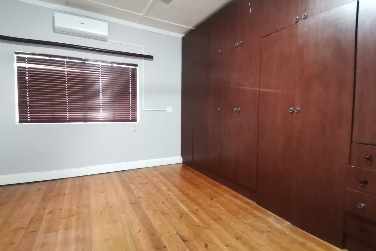 A spacious bedroom featuring polished hardwood flooring, extensive built-in wooden cabinetry, and a wall-mounted air conditioning unit.