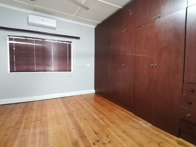 A spacious bedroom featuring polished hardwood flooring, extensive built-in wooden cabinetry, and a wall-mounted air conditioning unit.