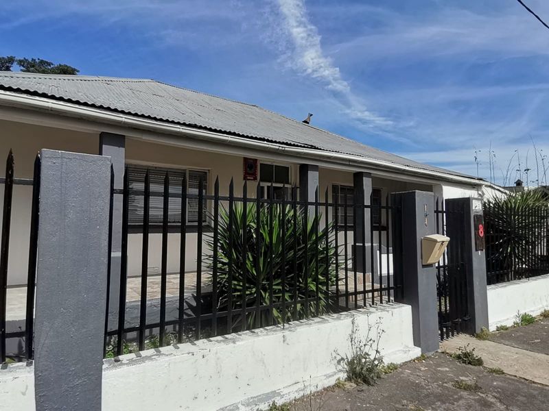 Front exterior view of a single-story house featuring a corrugated metal roof, covered porch, and secure wrought iron fencing with a masonry boundary wall.