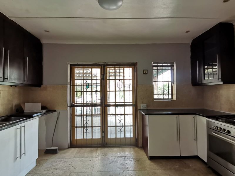 A functional kitchen featuring dark and white cabinetry, built-in oven with gas hob, and direct access to the outdoor area through a security gate.