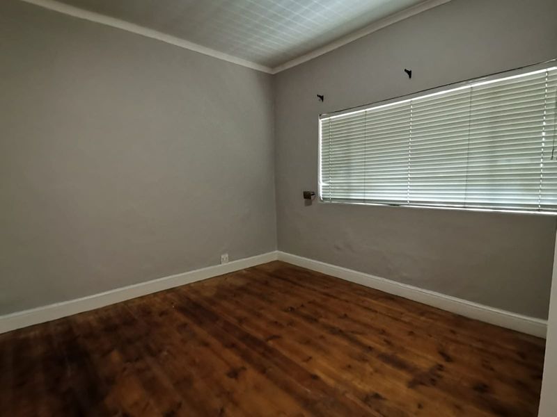 An empty bedroom featuring original timber flooring, neutral grey walls, and fitted venetian blinds, offering a blank canvas for renovation.
