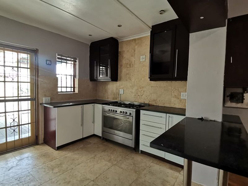 A functional kitchen featuring dark and white cabinetry, granite countertops, a gas stove, and stone tile finishes with direct access to the exterior.