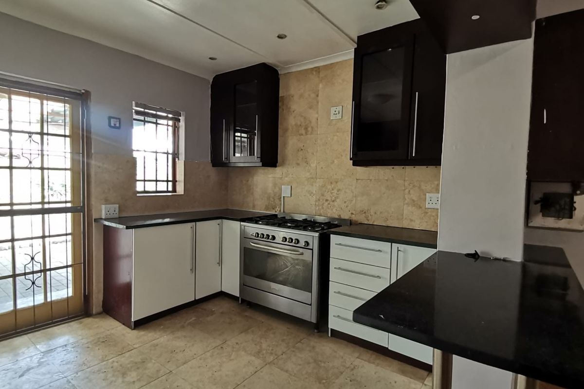 A functional kitchen featuring dark and white cabinetry, granite countertops, a gas stove, and stone tile finishes with direct access to the exterior.