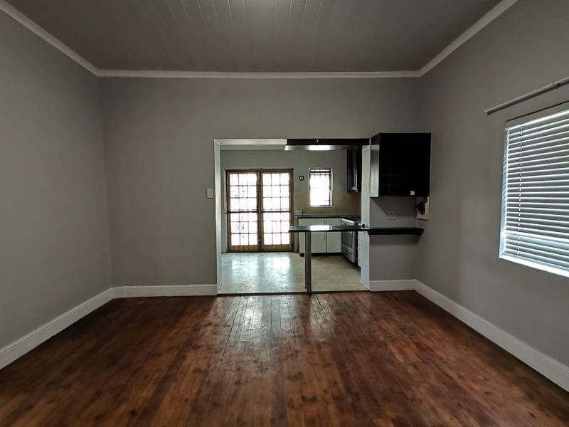 An open-plan living area featuring polished hardwood floors, a breakfast bar, and direct access to the kitchen and rear exterior through french doors.
