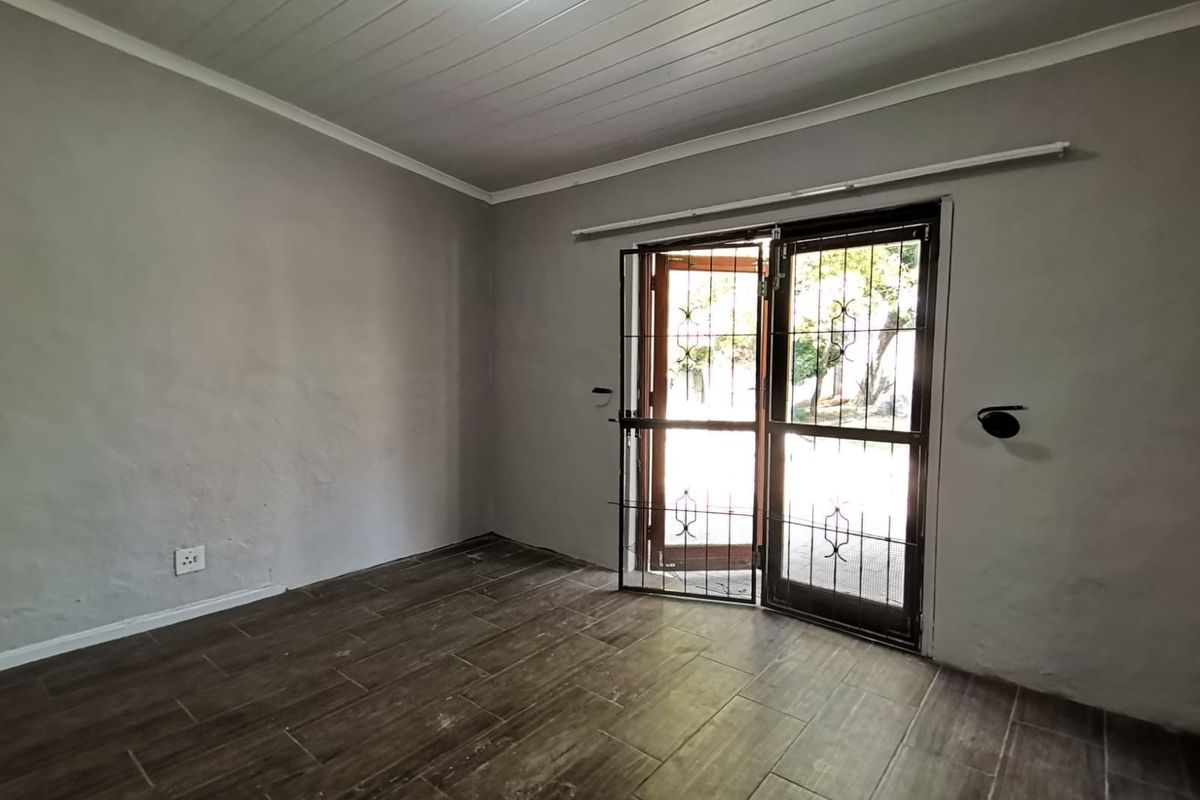 An empty living room featuring dark wood-look floor tiles, a white timber-look ceiling, and double doors leading to the exterior with a security gate.