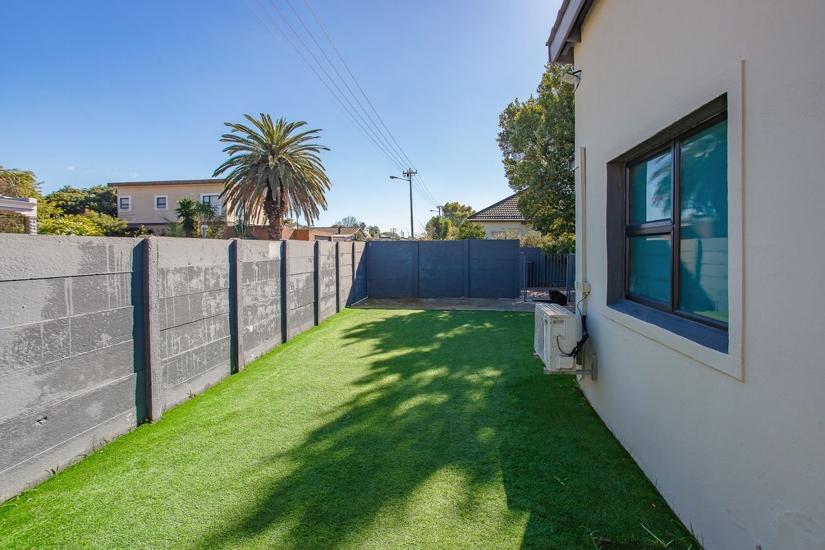 A private rear garden featuring a low-maintenance artificial lawn, enclosed by a secure precast concrete boundary wall with an external air conditioning unit.