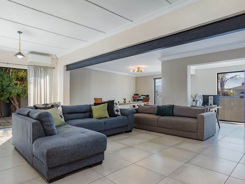 Spacious open-plan living area featuring tiled floors, an exposed structural steel beam, and direct access to the outdoor patio through sliding glass doors.