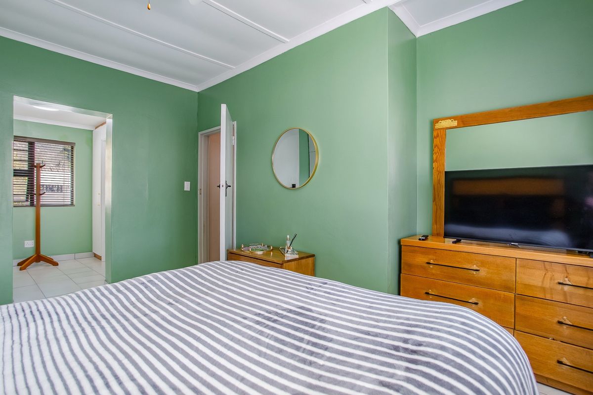 A bedroom featuring green painted walls, a ceiling fan, and an adjoining space visible through the doorway.