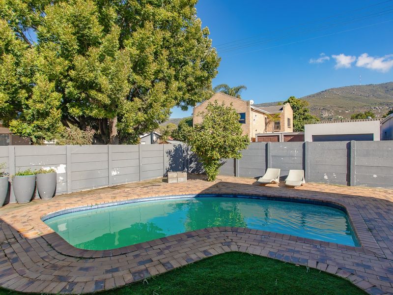 Outdoor pool area featuring a swimming pool, brick paved surround, artificial lawn, and a perimeter boundary wall.