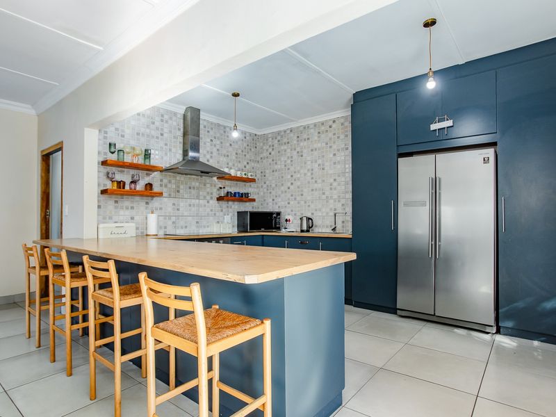 Modern kitchen featuring a central island with a wooden countertop, mosaic tile backsplash, dark blue cabinetry, and tiled flooring.