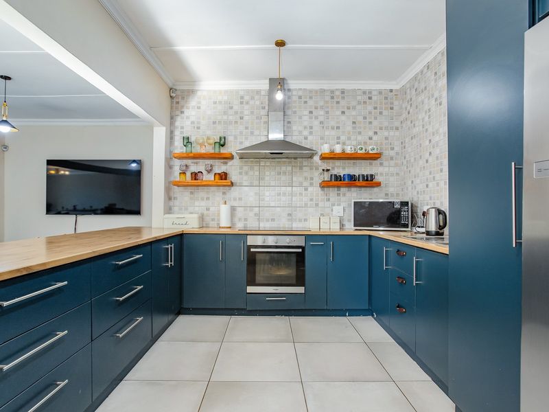 Modern kitchen featuring blue cabinetry, wooden countertops, tiled backsplash, built-in oven, and extractor fan, offering a functional and stylish cooking space.
