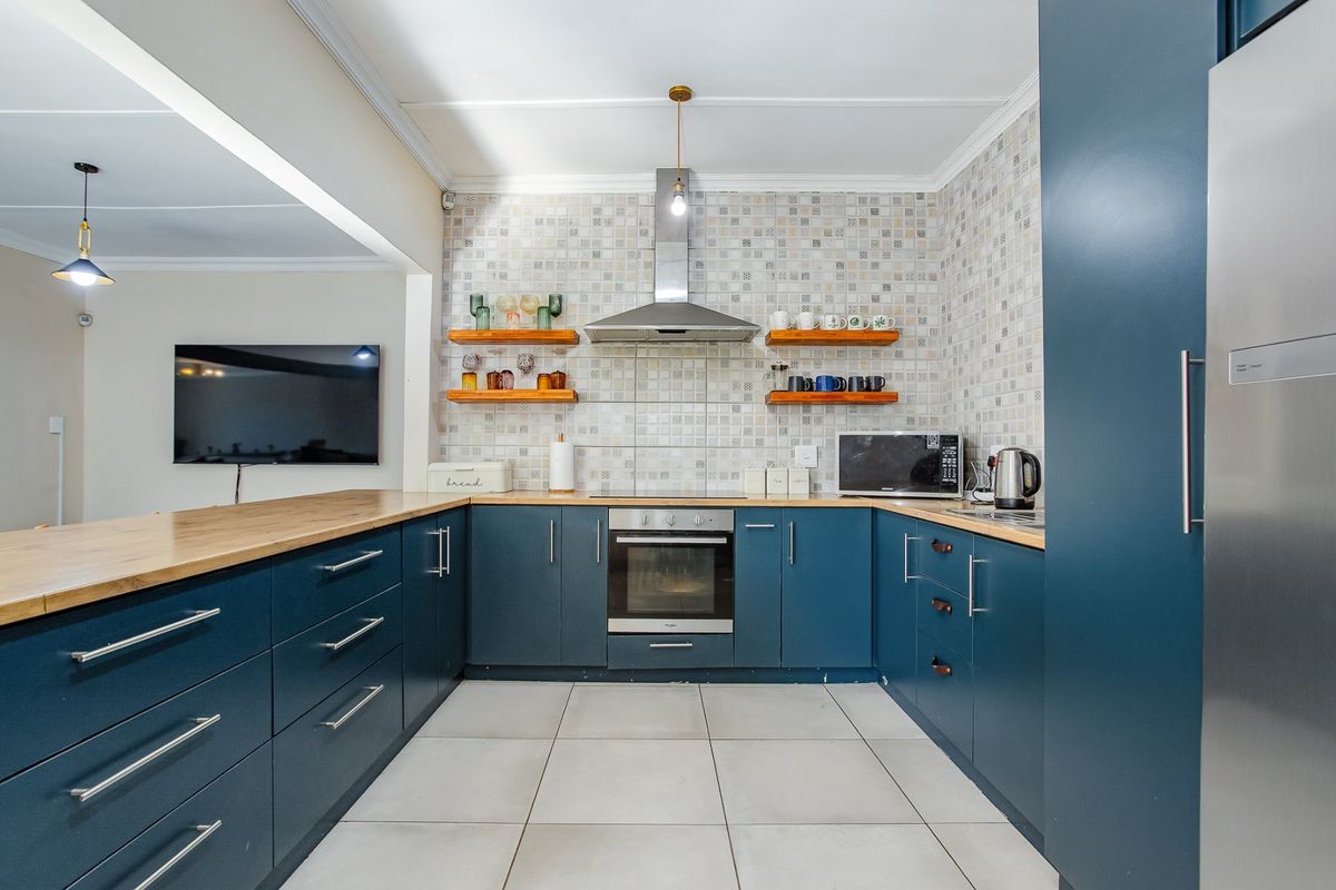 Modern kitchen featuring blue cabinetry, wooden countertops, tiled backsplash, built-in oven, and extractor fan, offering a functional and stylish cooking space.