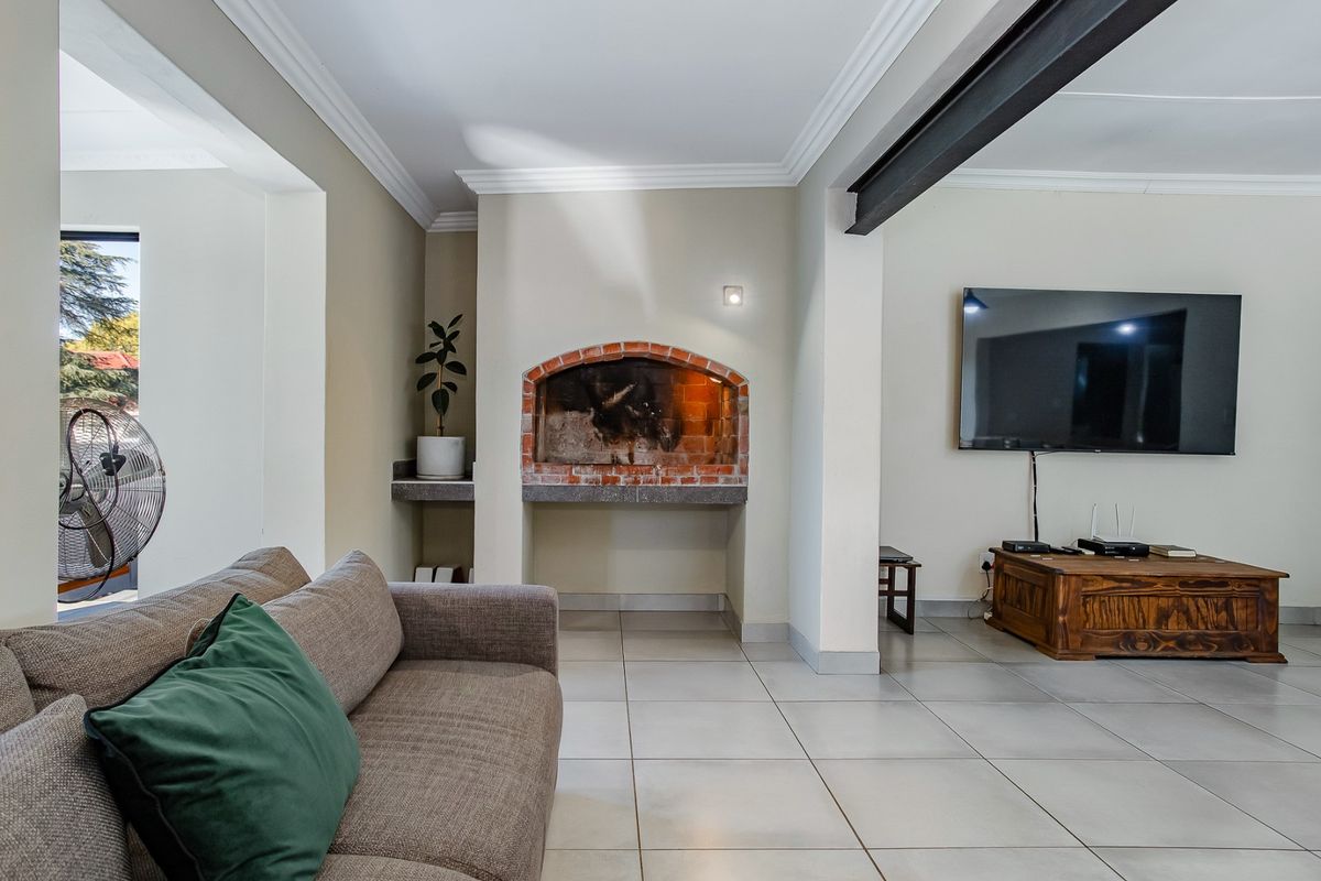 Spacious living room featuring a classic brick fireplace, neutral tiled flooring, and an exposed steel beam, creating a comfortable and functional living space.