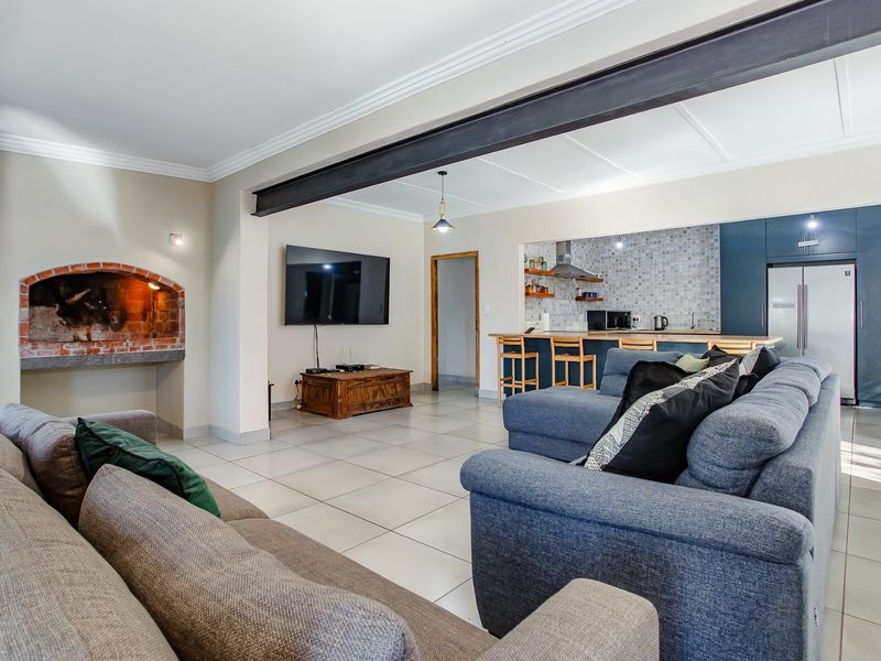 Spacious open-plan living area featuring a brick fireplace, exposed steel beam, and a modern kitchen with a breakfast bar and mosaic backsplash.