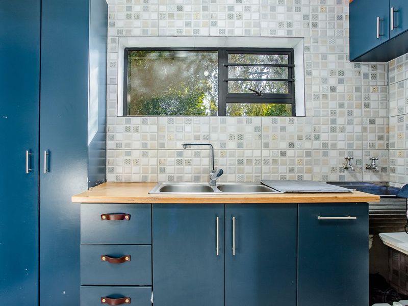 A compact kitchen area featuring blue built-in cabinetry, a timber countertop, double bowl sink, and a decorative mosaic tile backsplash.