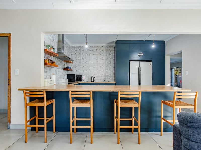Modern kitchen featuring dark blue cabinetry, a wooden breakfast bar, and a mosaic tile backsplash, seamlessly integrated into the open-plan living space.