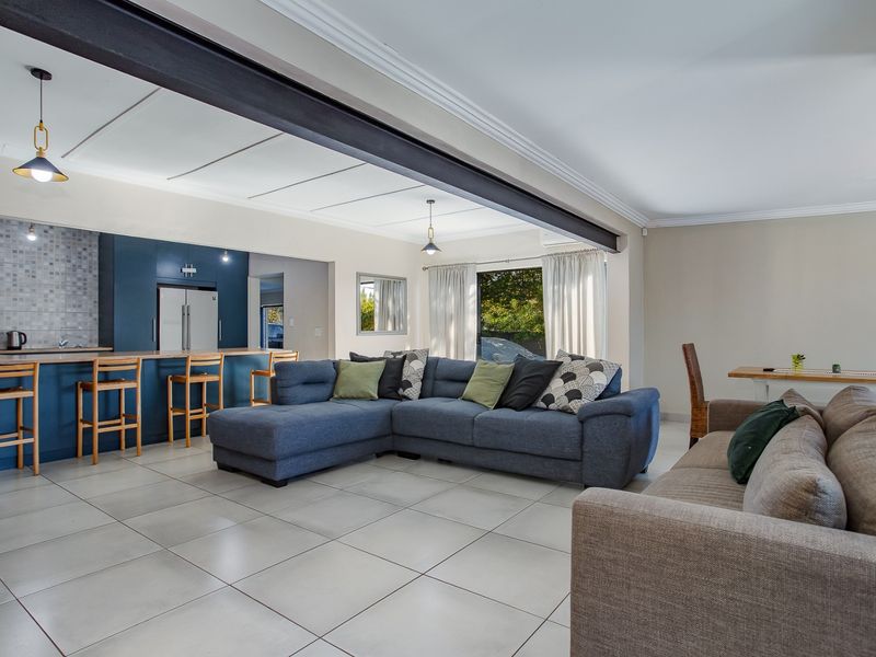 Spacious open-plan living area featuring a modern kitchen with a breakfast island, tiled floors, and an exposed structural beam, creating a bright, functional layout.