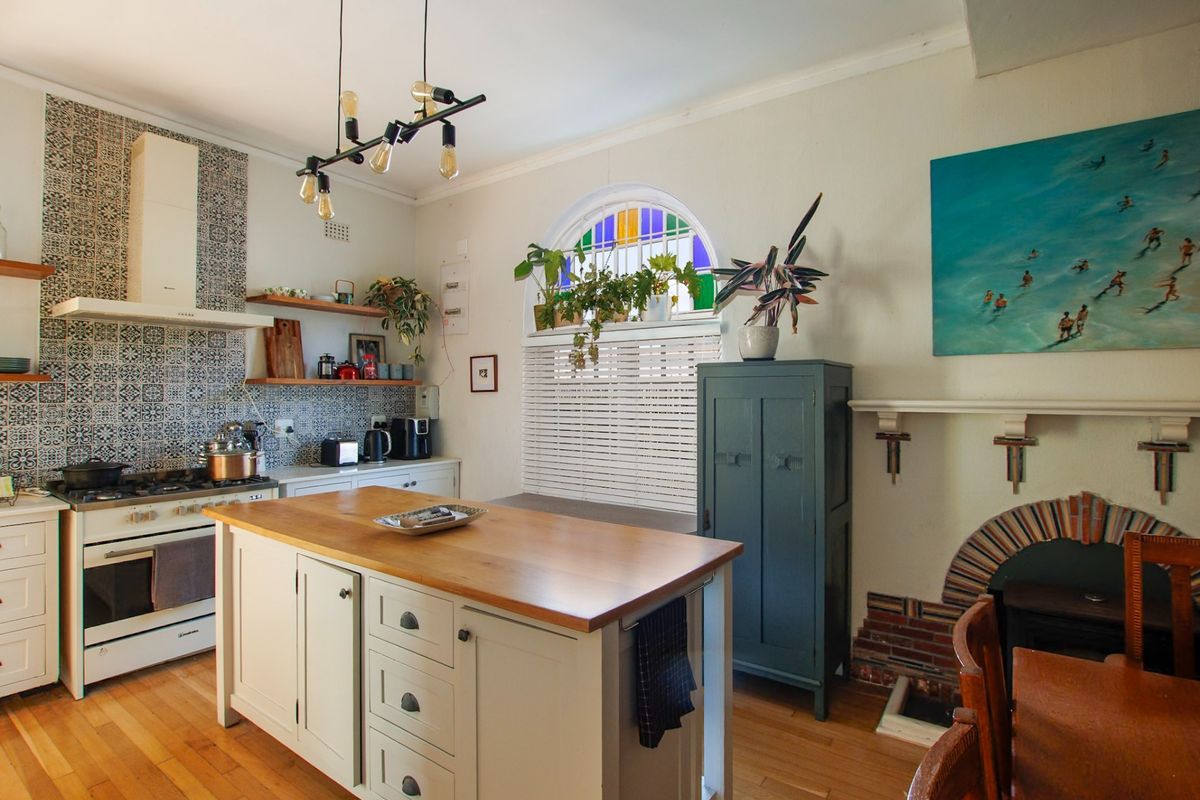 A charming kitchen featuring a central island with wooden countertop, gas stove, decorative tiled backsplash, and a unique arched window with stained glass accents.