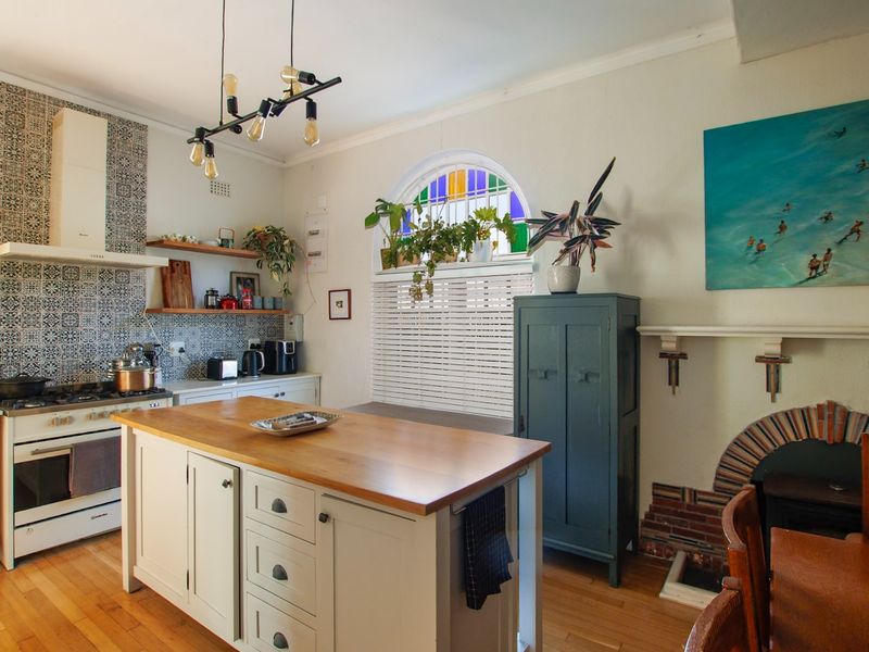 A charming kitchen featuring a central island with wooden countertop, gas stove, decorative tiled backsplash, and a unique arched window with stained glass accents.