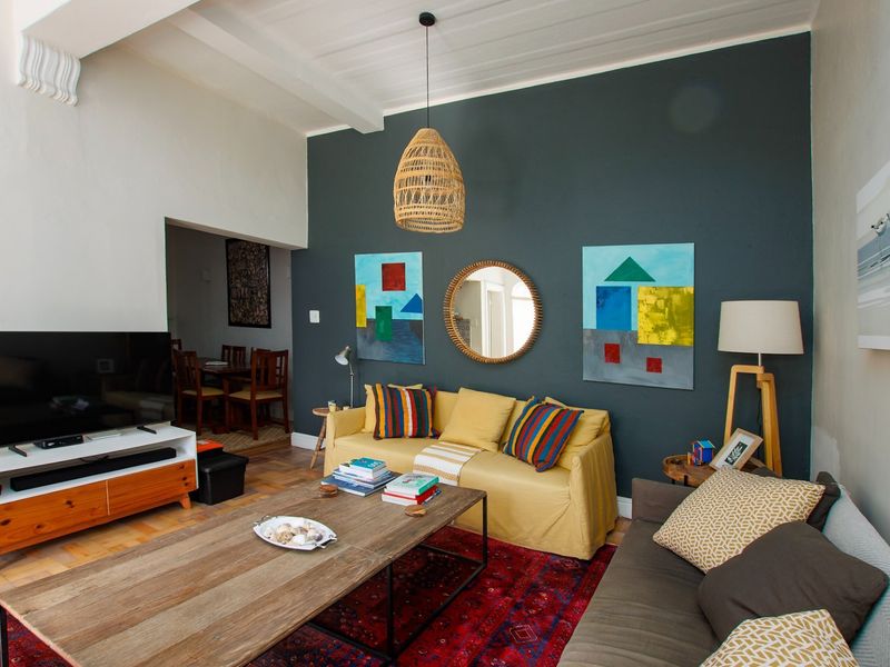 A cozy living room featuring dark accent walls, parquet flooring, and exposed ceiling beams, with an open flow into the adjacent dining area.