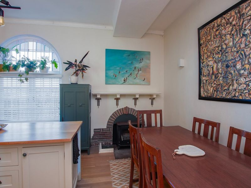 Dining area featuring hardwood flooring, a built-in fireplace with brick detailing, and an arched window, adjacent to a kitchen island.
