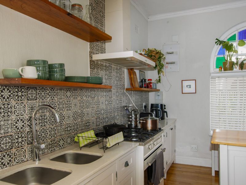A well-appointed kitchen featuring a gas hob, extractor fan, double bowl sink, patterned tile splashback, and timber floating shelves under an arched window.