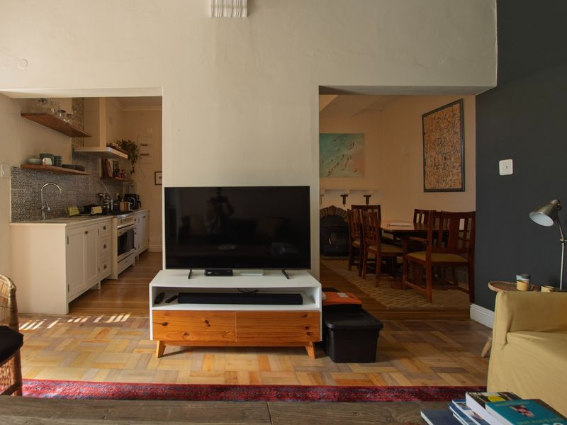 Open-plan living area featuring classic parquet flooring, connecting to a functional kitchen and a separate dining space with a fireplace.