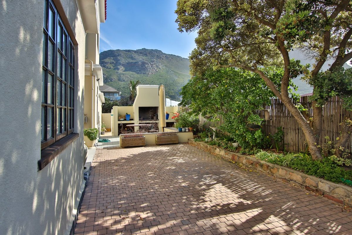 A private rear courtyard featuring a paved patio area, built-in braai, and established garden borders with mountain views.