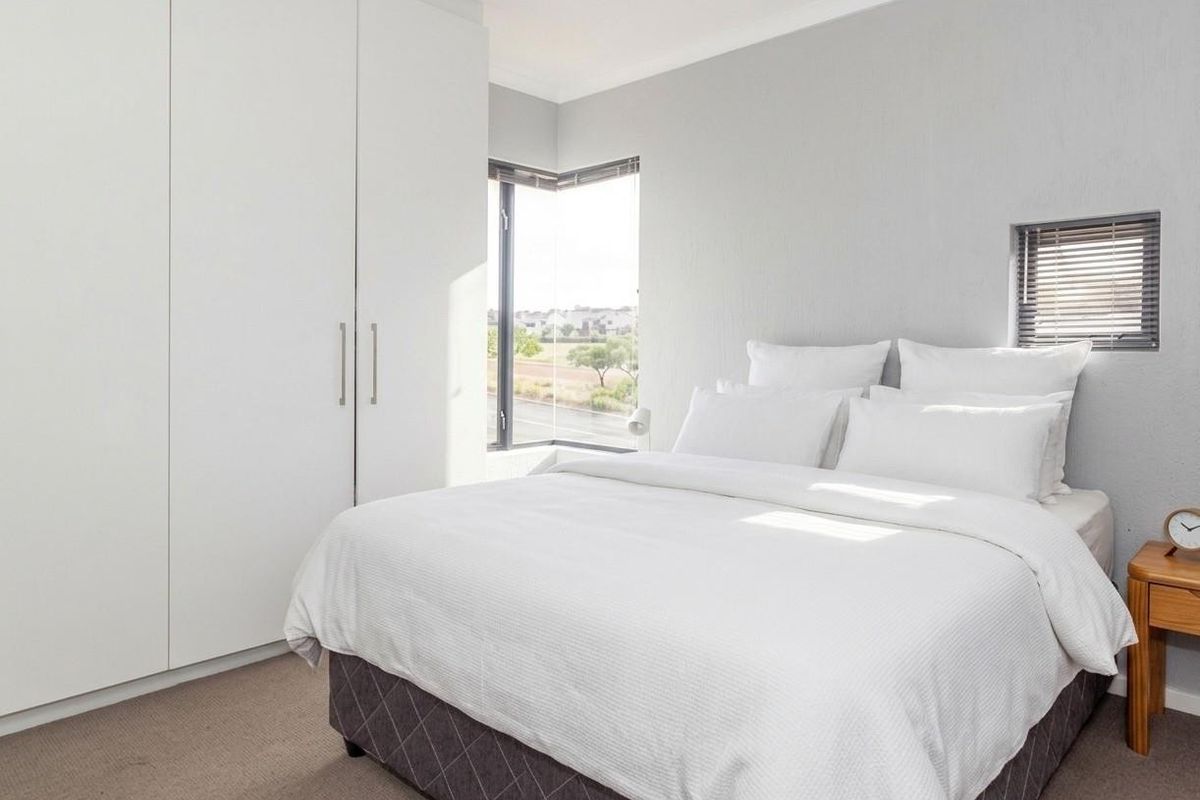 A bright bedroom featuring built-in cupboards, neutral carpeting, and a corner window providing natural light and exterior views.