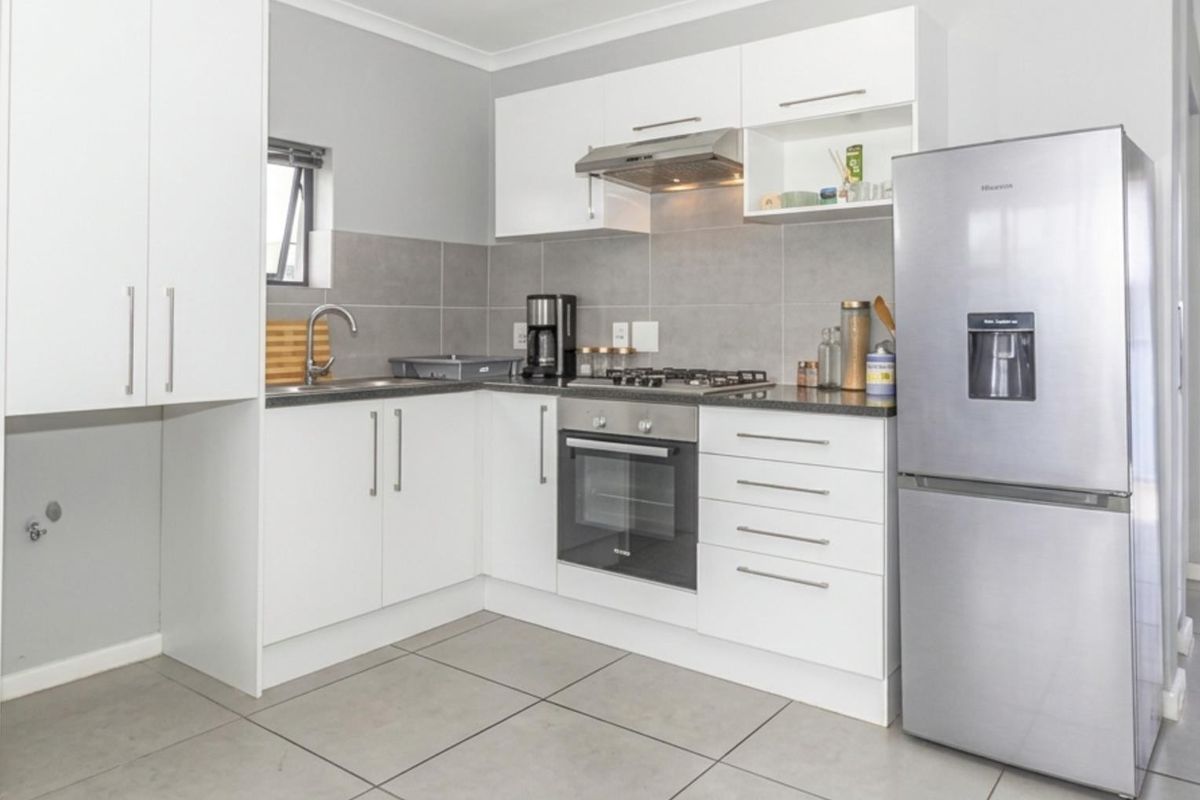 Modern kitchen featuring white cabinetry, stainless steel appliances, gas hob, built-in oven, extractor fan, and neutral tiled splashback and flooring.