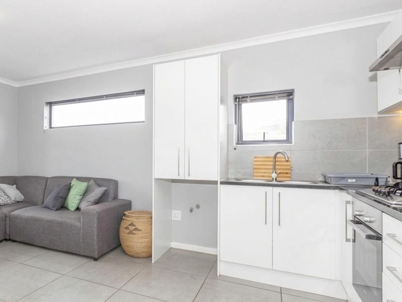 Modern open-plan living area featuring a compact kitchen with built-in cabinetry, stainless steel appliances, and tiled flooring throughout.